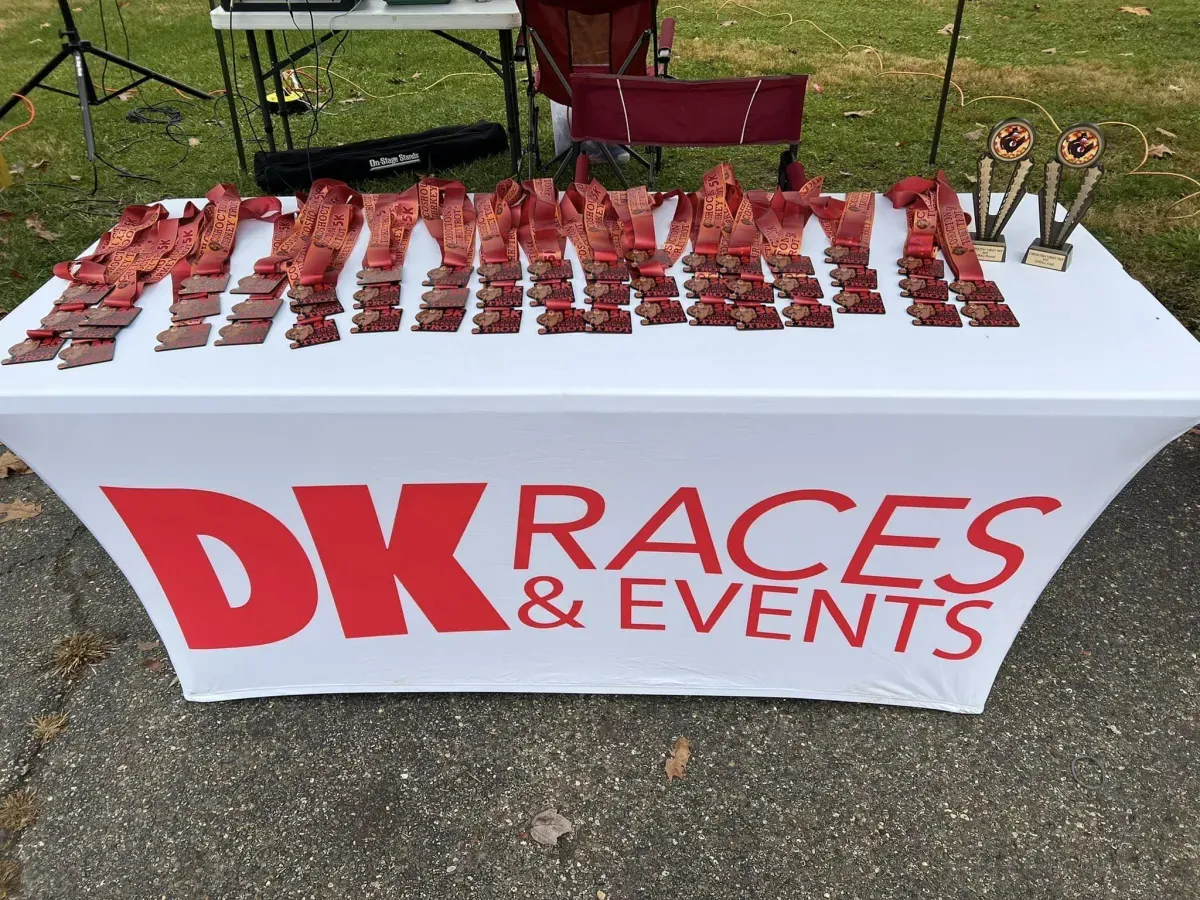 A table covered with a white cloth displaying numerous race medals and two trophies, suggesting awards for race participants.