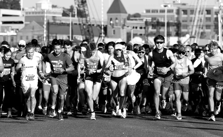 A group of runners in the foreground, starting a race, with a blurred urban background.