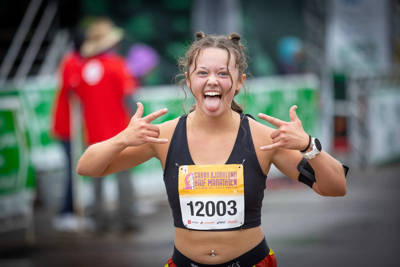 A young woman with her tongue out and hands in a rock-and-roll gesture, wearing a race bib for the Garry Bjorklund Half Marathon.
