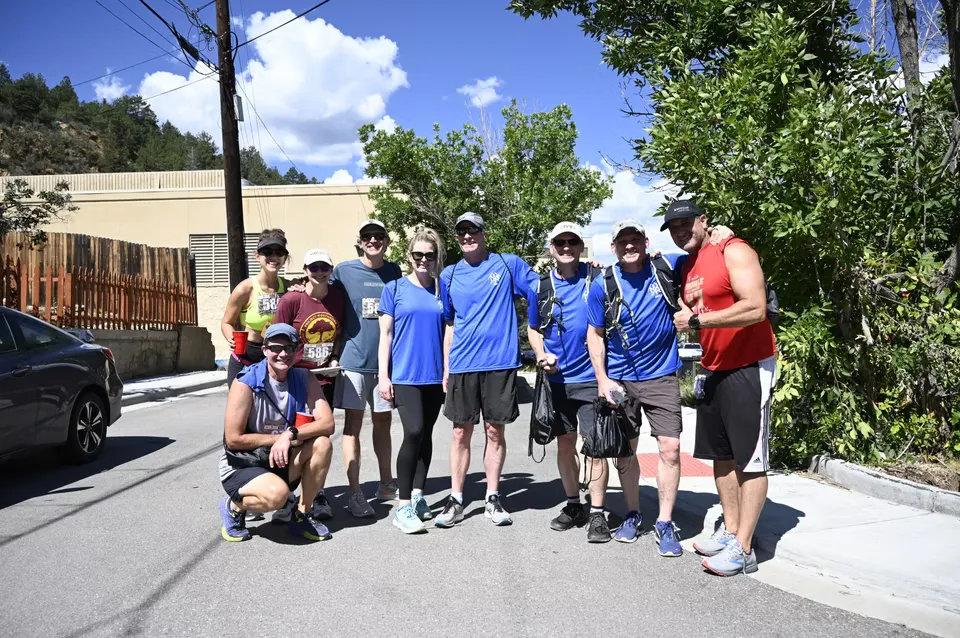 A group of runners posing for a photo on a street, with trees and buildings in the background.