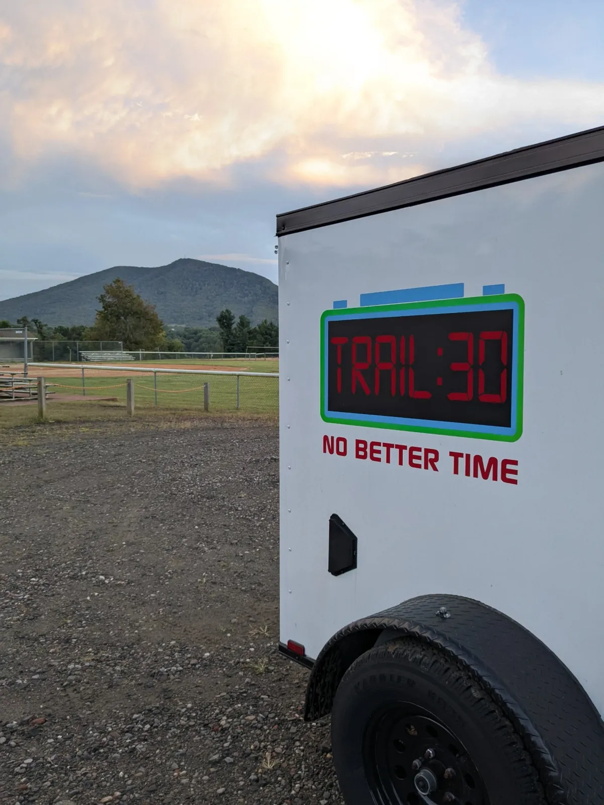 A trailer with 'TRAIL 30 NO BETTER TIME' displayed on its side, with a scenic mountain view in the background.