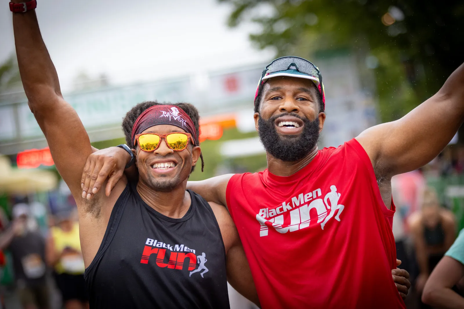 Two smiling male runners with arms around each other, celebrating at a race.