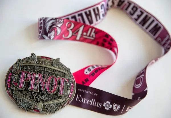 A close-up of a race medal and its ribbon, featuring the text 'Wineglass Challenge Pinot 34.1k'.