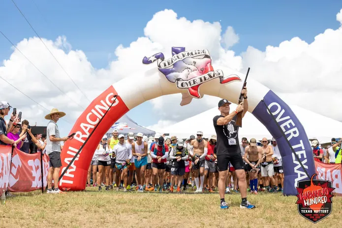 Runners gathered at the start line under an inflatable arch, with a man holding a rifle to signal the start of the Habanero Hundred race.