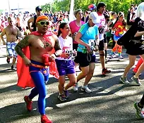 Runners in a race, one dressed as a superhero, with a crowd in the background.