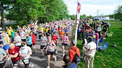 A large group of runners are starting a race on a paved road, with spectators on the side.