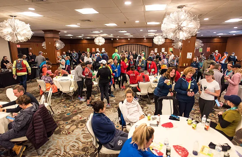 Runners gathered indoors after a race, socializing around tables and holding drinks.