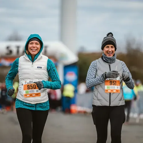 Two women smiling at the start line of a half marathon.