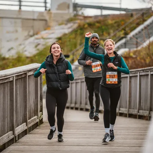 Two women and a man running on a wooden boardwalk, with the woman in the foreground raising her fist in celebration.