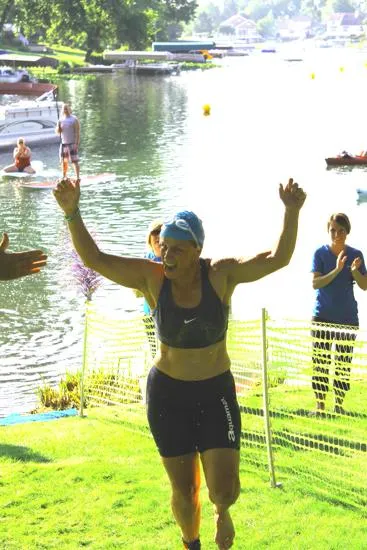 A female runner with arms raised in victory crosses the finish line near a body of water.