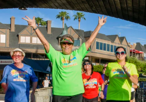 A group of runners, some with arms raised in celebration, run towards the camera on a sunny day.