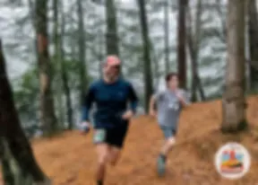 Two runners, one adult and one child, running on a wooded trail.