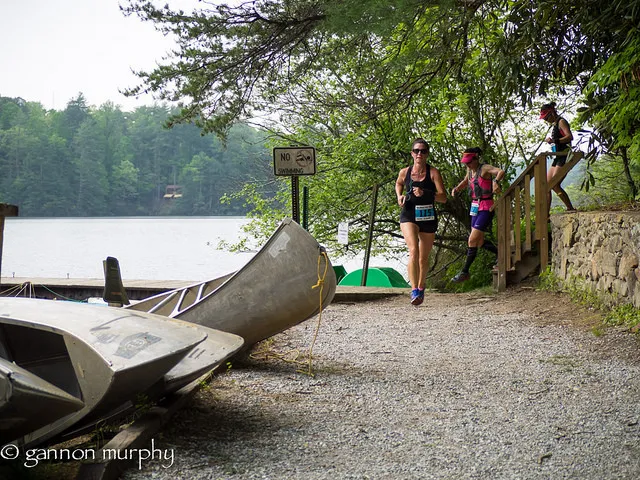 Runners on a trail near a lake, with canoes in the foreground.