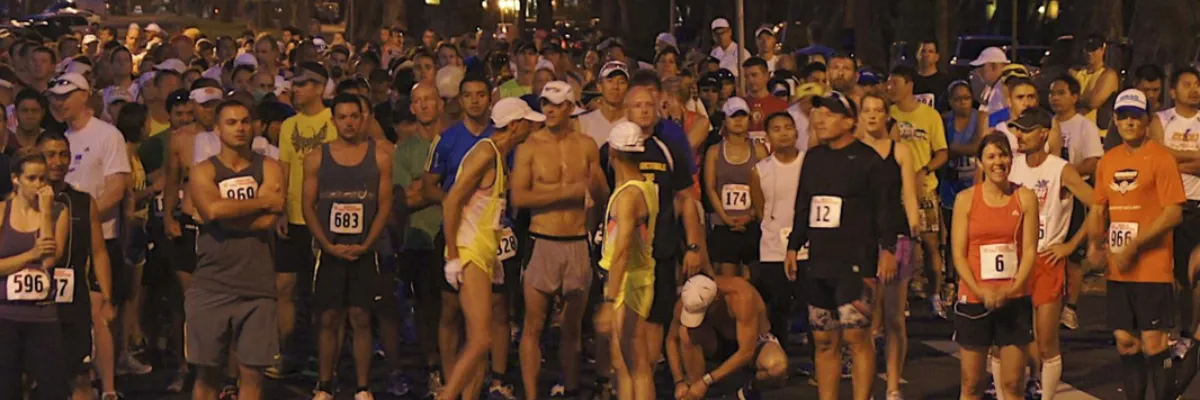 A large crowd of runners gathered at the start line of a race, many wearing bib numbers.