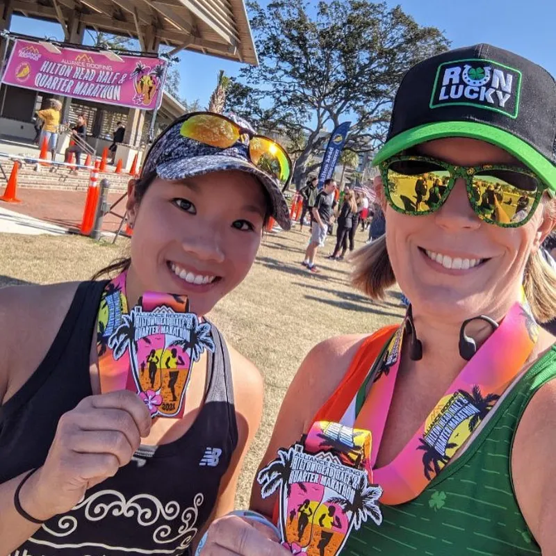 Two smiling women proudly display their race medals after completing the Hilton Head Half & Quarter Marathon.