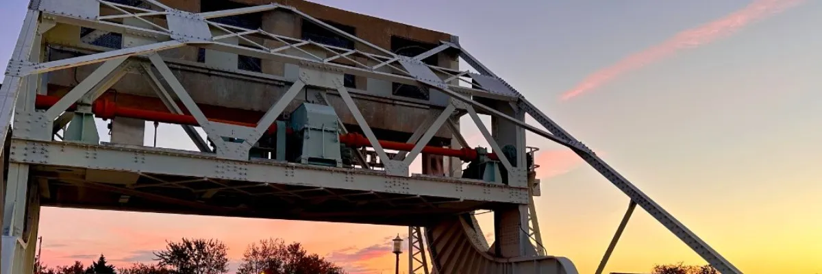 A drawbridge structure against a sunset sky with pink clouds.