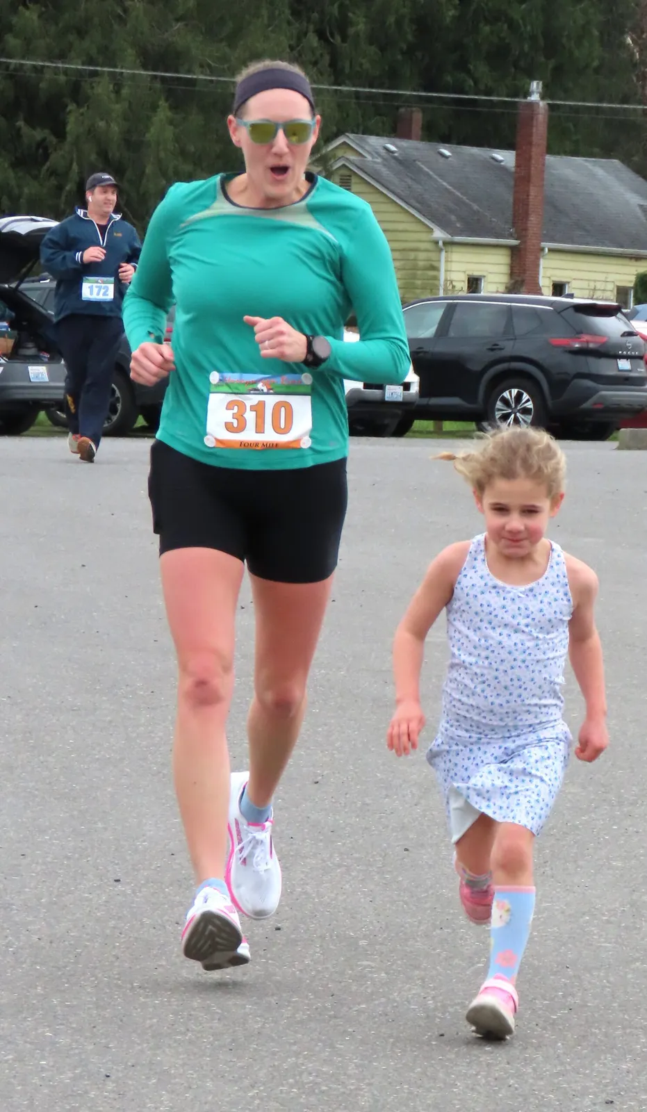 A woman and a young girl running side-by-side in a race, with another runner in the background.
