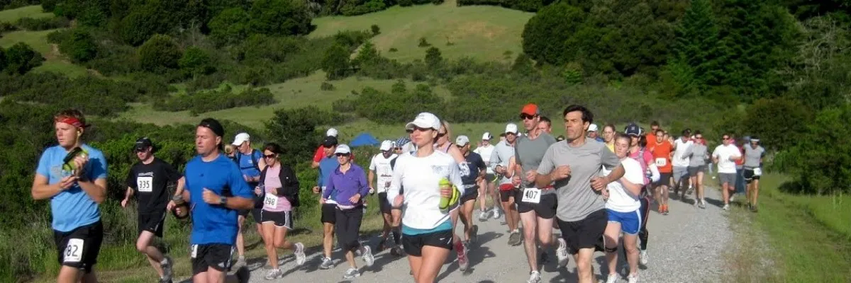 A group of runners on a gravel path surrounded by green hills and trees.
