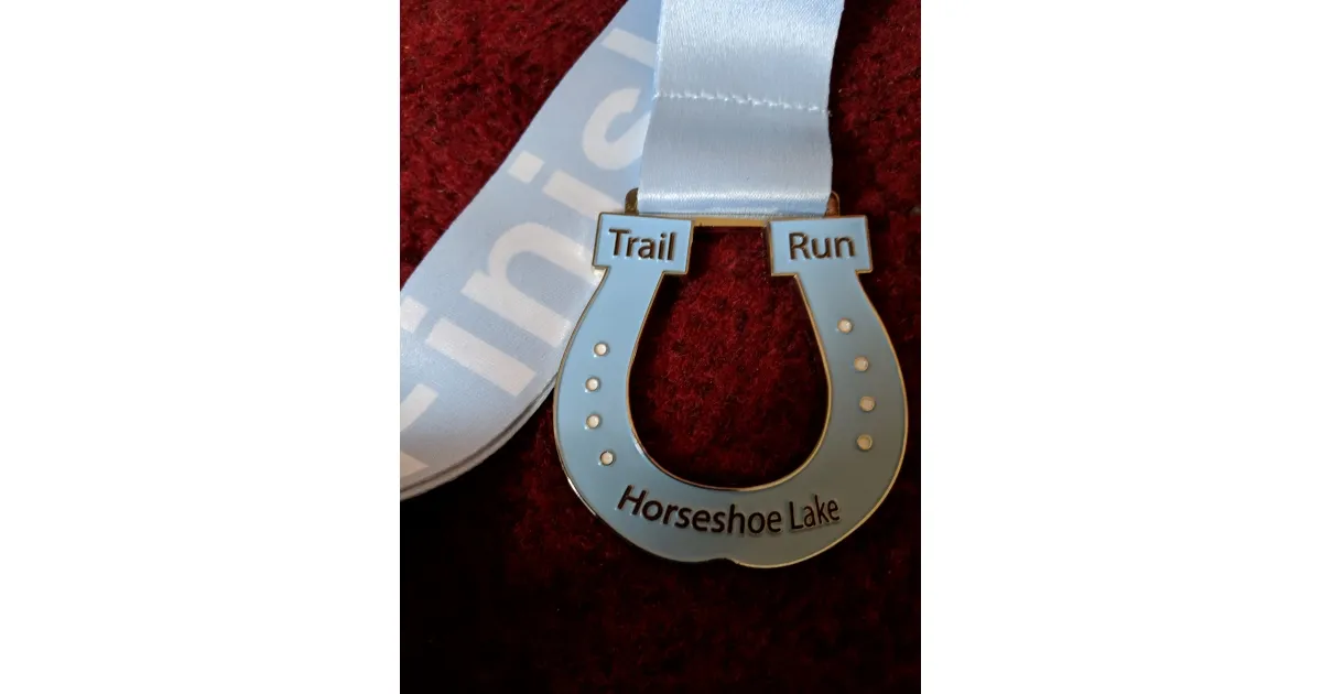 A horseshoe-shaped medal with 'Trail Run' and 'Horseshoe Lake' inscribed on it, on a light blue ribbon.