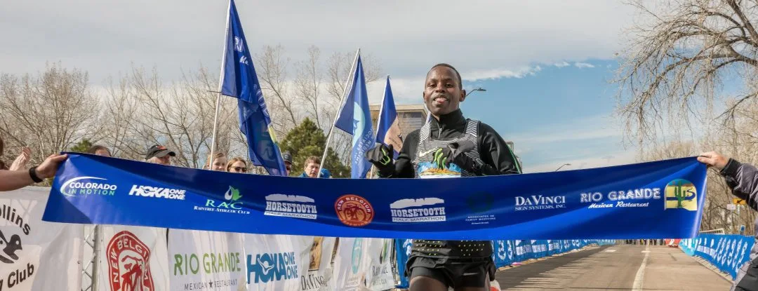 A male runner smiles as he crosses the finish line, holding a banner with race sponsors.