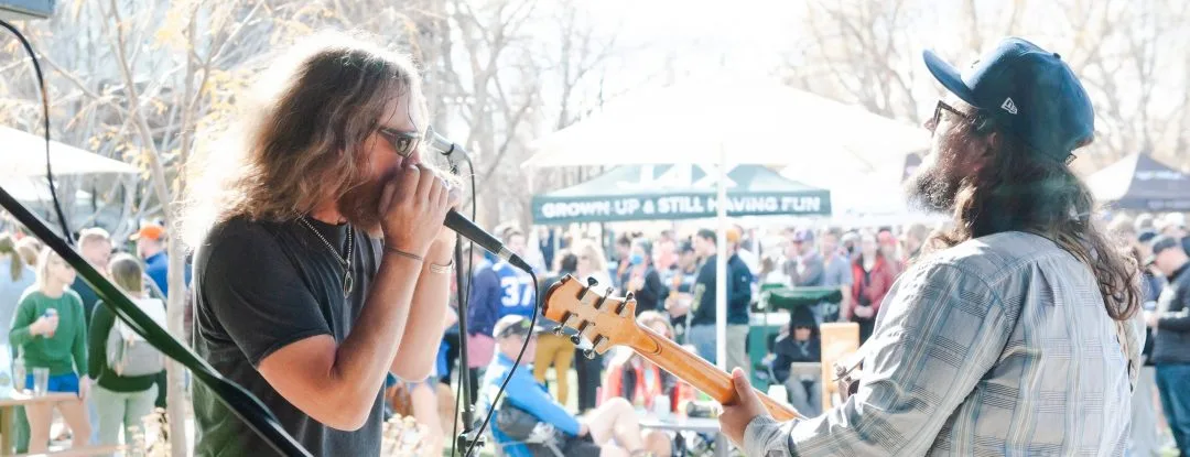 A band performs on a stage with a crowd of people in the background at an outdoor event.