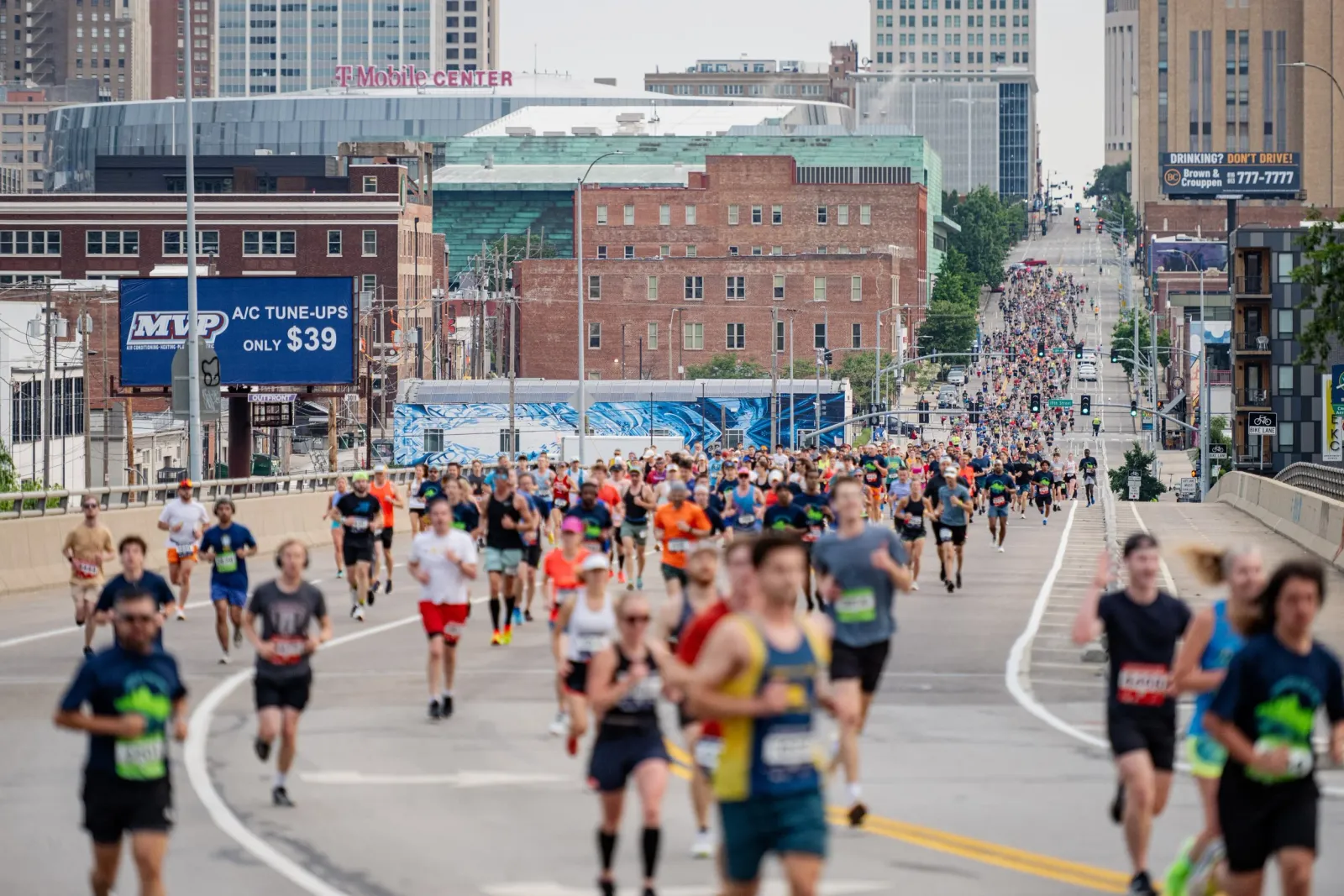 A large group of runners participating in a race on an urban street, with city buildings in the background.