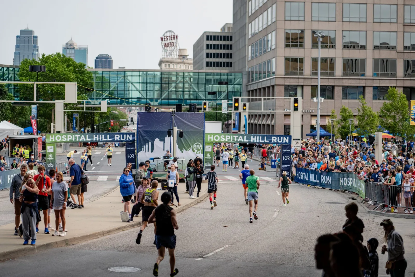Runners crossing the finish line at the Hospital Hill Run with a large crowd watching and city buildings in the background.