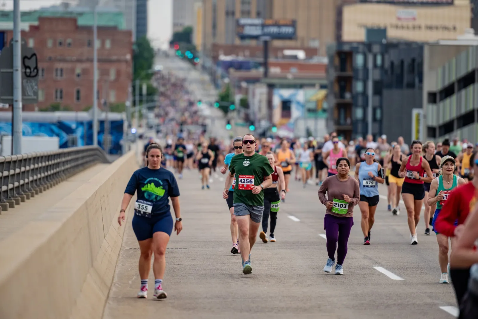 Runners participating in the Hospital Hill Run on a city street, with buildings and a crowd visible in the background.