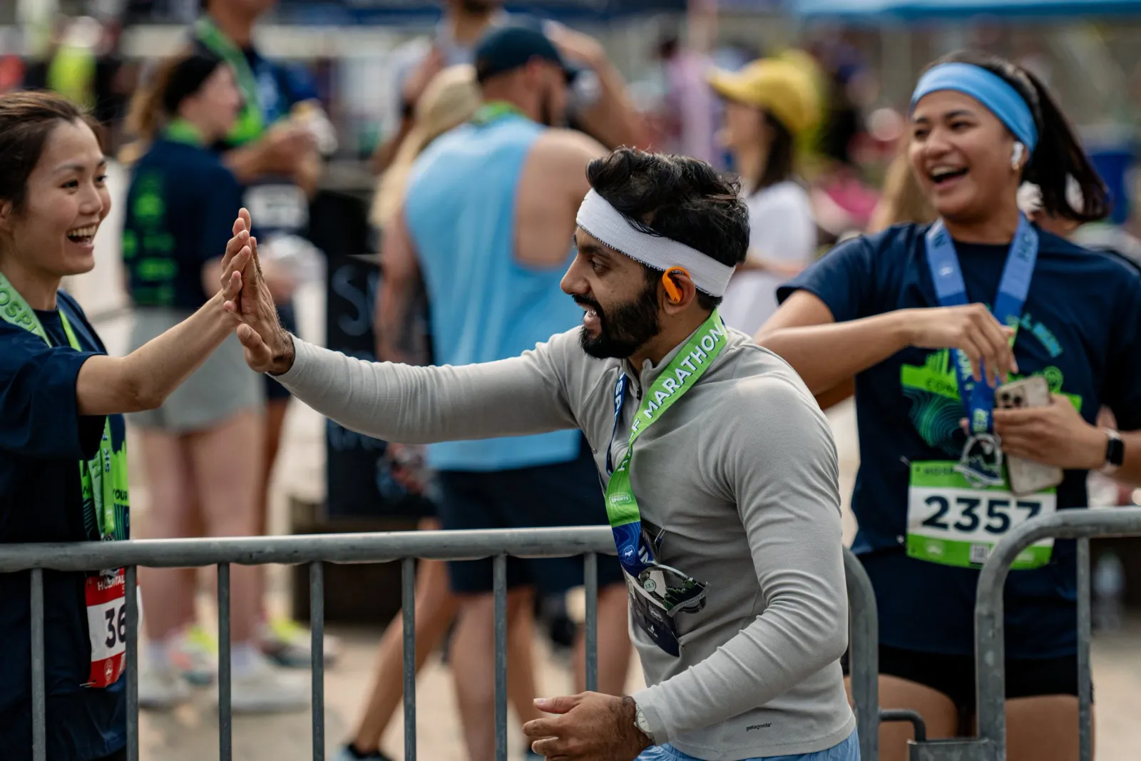 Two runners, a woman and a man, smiling and giving each other a high-five at a race, with other runners and spectators in the background.