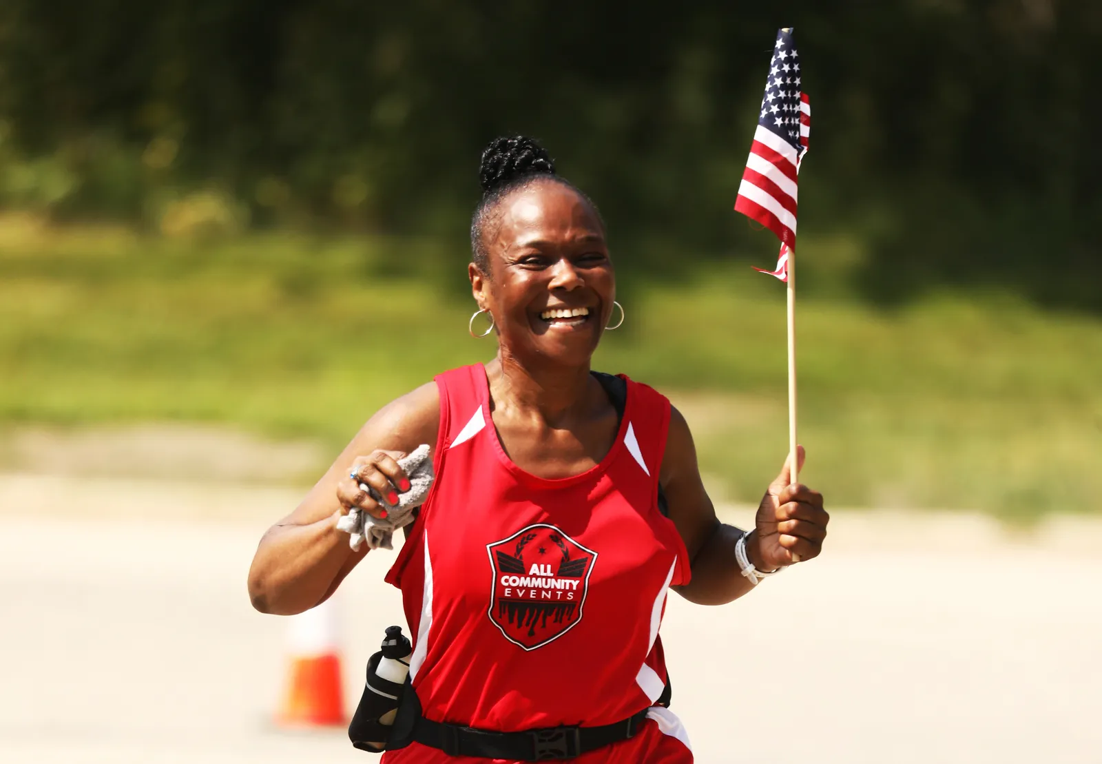 A smiling woman runs with an American flag at the finish line of a race.