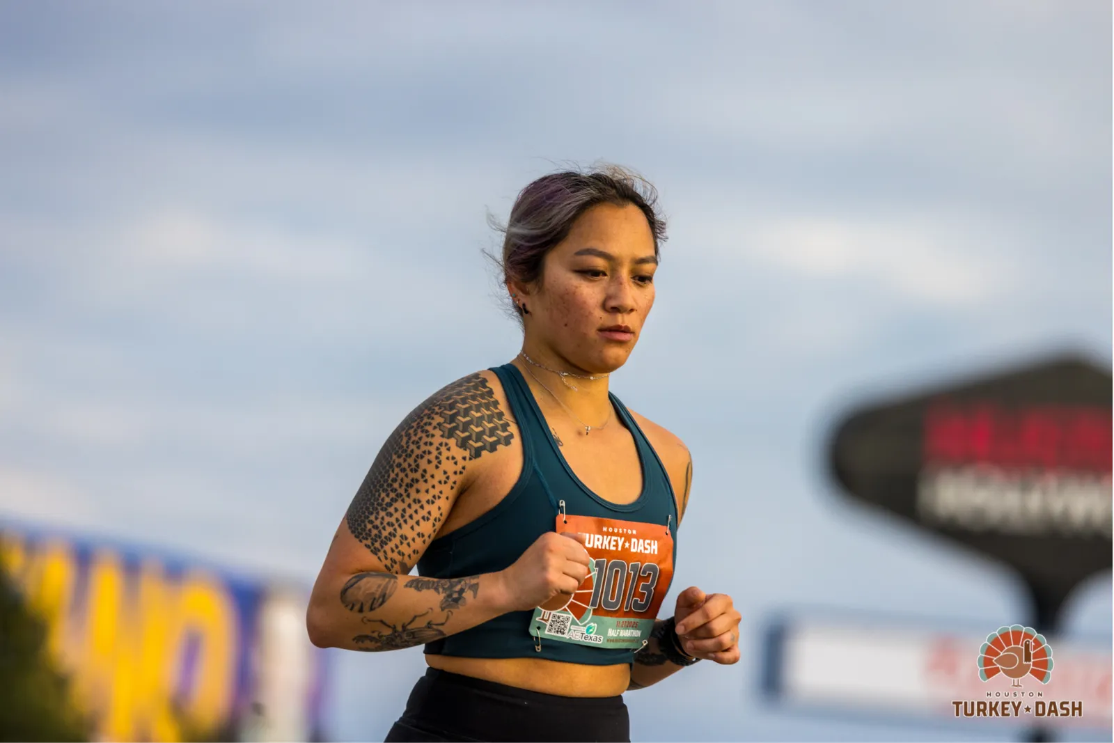 A female runner with tattoos on her arm and a race bib numbered 1013 runs during the Houston Turkey Dash.