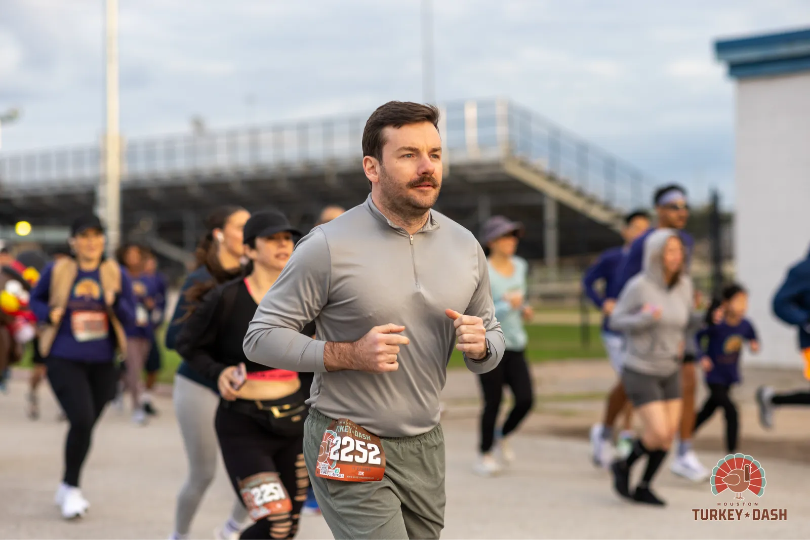 A man in a grey shirt runs forward with a group of other runners behind him at the Houston Turkey Dash.
