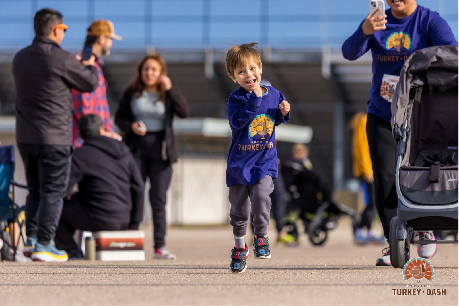 A young boy in a purple Turkey Dash t-shirt runs towards the camera with a huge smile, his arms pumping.