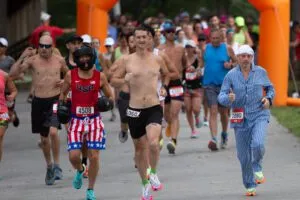 Runners in costumes and athletic wear start a race under an orange archway.
