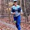 A female runner smiles as she runs on a wooded trail during the Huff n' Puff Half Marathon.