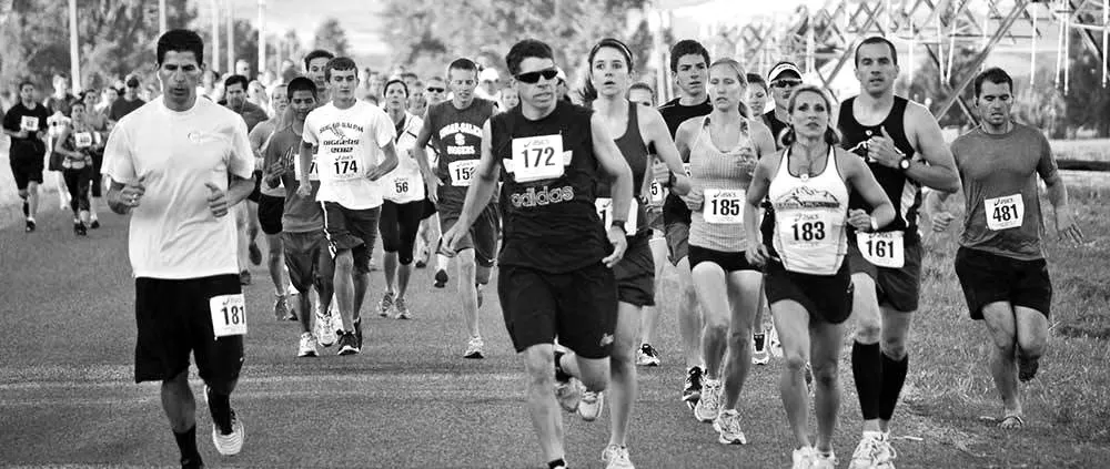 A group of runners in a race, with bib numbers visible, running on a road.
