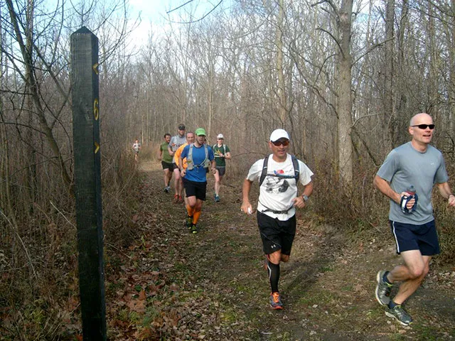 A group of men running on a wooded trail during a race.