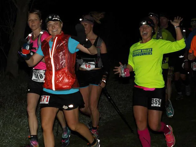 A group of female runners smiling and waving at the camera during a night race, with bib numbers visible.