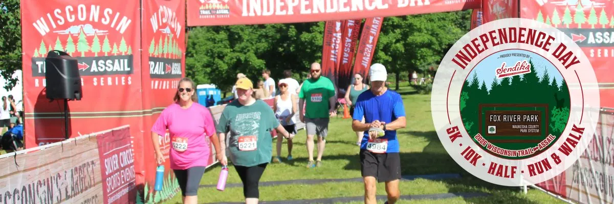 Runners crossing the start/finish line at the Independence Day Run, with banners and cheering crowds in the background.