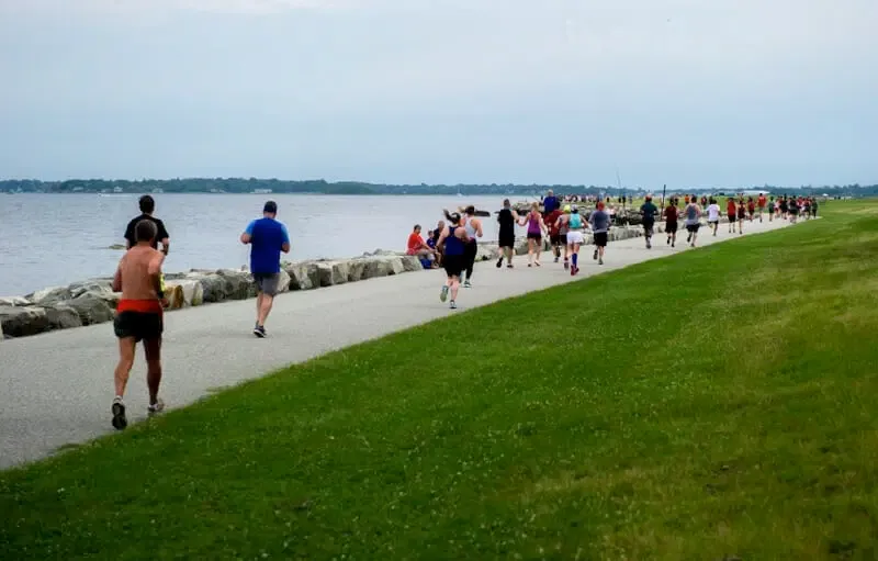 Runners on a paved path alongside a waterfront during a race.