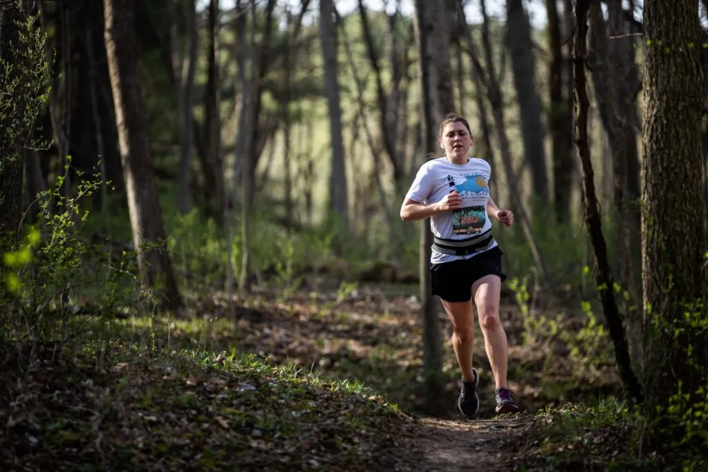 A female runner runs on a dirt trail through a forest.
