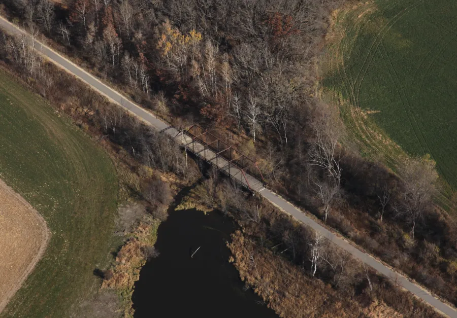 Aerial view of a road crossing a bridge over a dark body of water, surrounded by trees and fields.