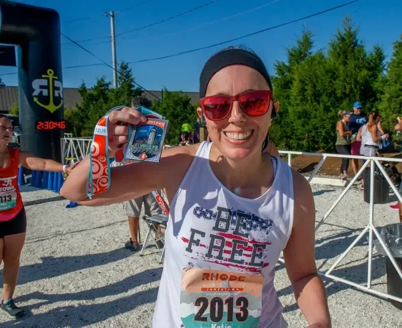 A smiling female runner at the finish line, holding up her race medal.