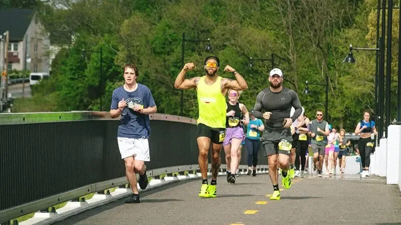 Runners on a bridge during a race, with one runner flexing his biceps.
