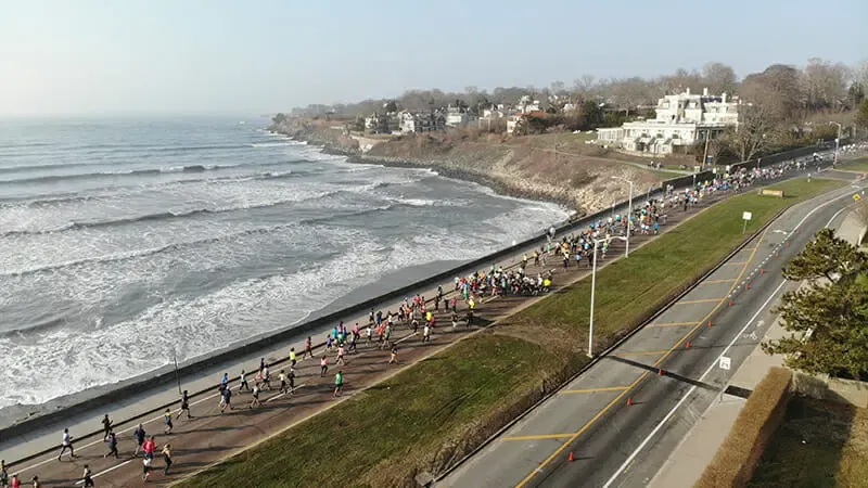 A drone view of a half marathon with many runners on a road next to the ocean.