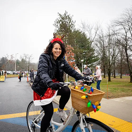 A woman wearing a Santa hat and a sequined skirt rides a bicycle decorated with Christmas lights.