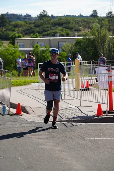 A male runner with a prosthetic leg smiles and gives a thumbs up while running on a road course.