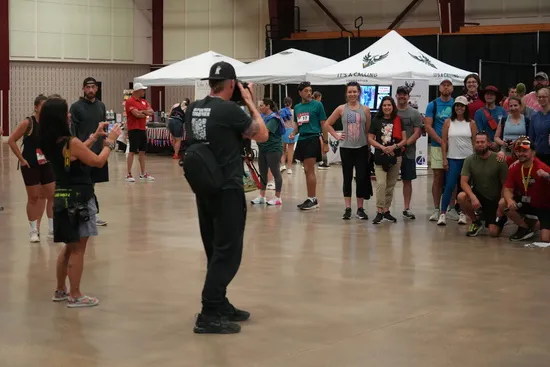 A group of people posing for a photo at an indoor race event, with tents and event signage in the background.