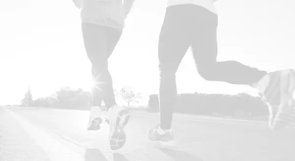 Two runners seen from behind, running on a road with the sun shining.