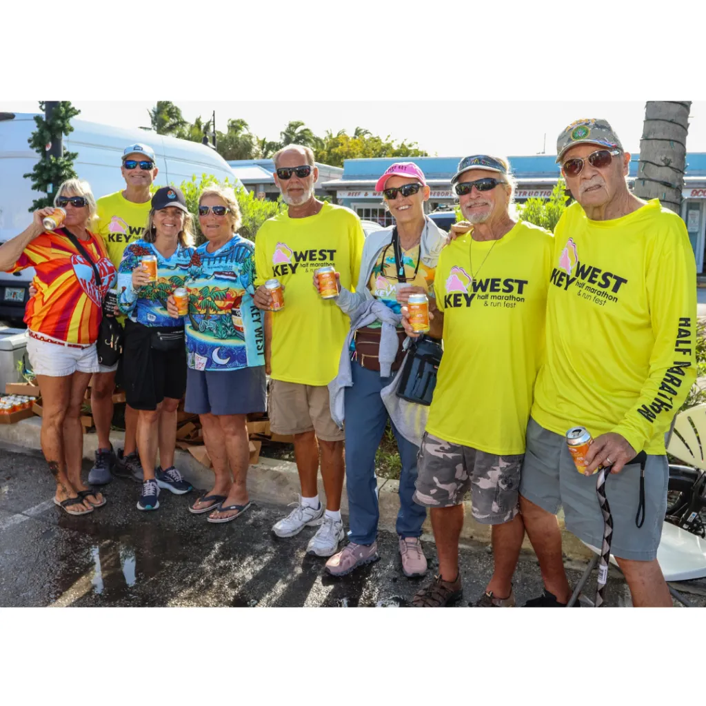 A group of people wearing yellow Key West Half Marathon t-shirts and holding drinks, smiling and posing for a photo.